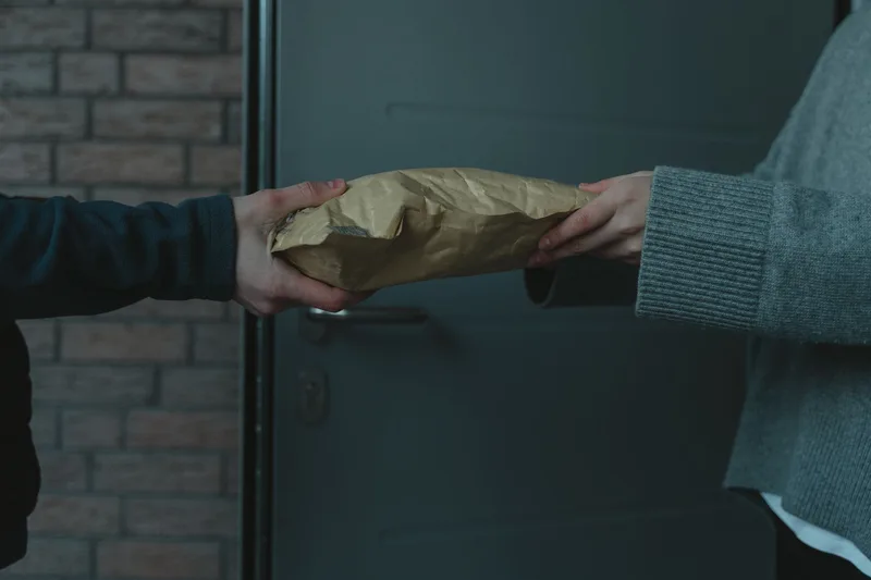 A parcel changes hands at the doorstep between courier and customer, the final step before cash payment is collected