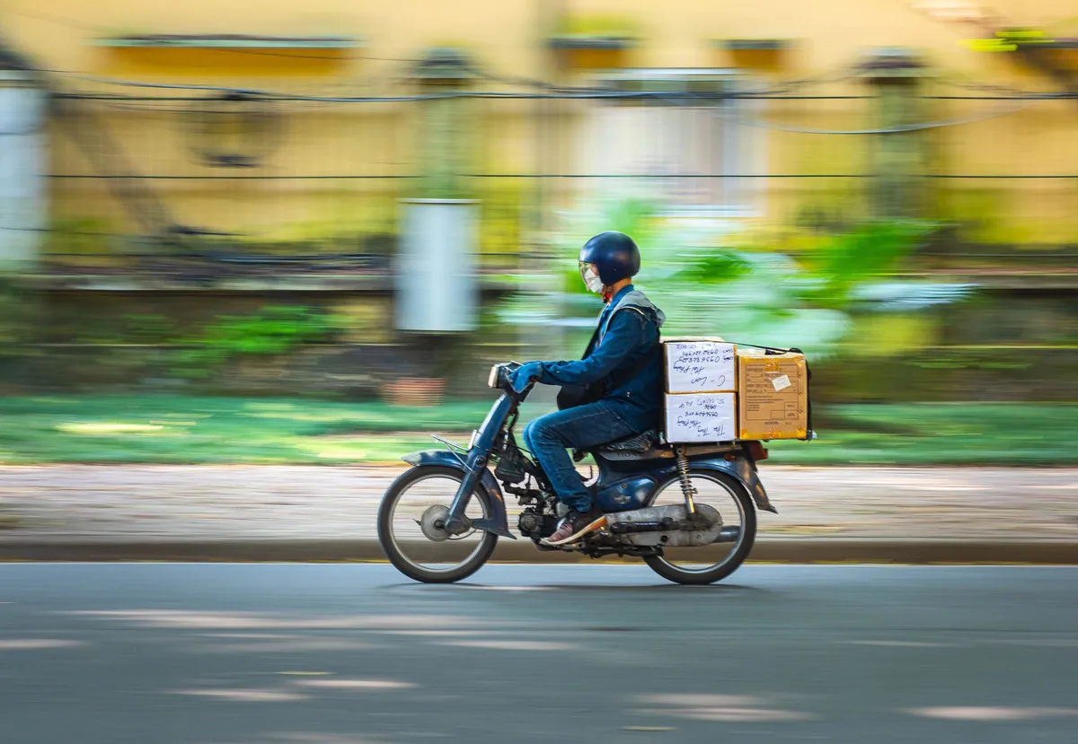 Motorcycle courier rider speeding down a road delivering parcels, motion blur background