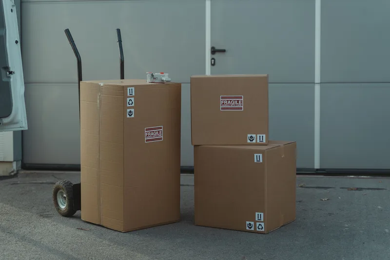 Cardboard boxes stacked on a dolly outside a warehouse, ready for courier pickup