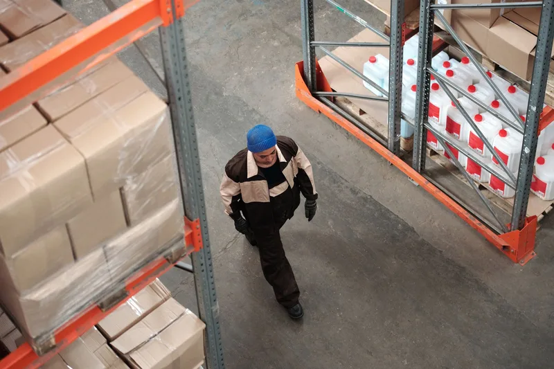 Warehouse worker walking past stacked ecommerce packages ready for courier pickup